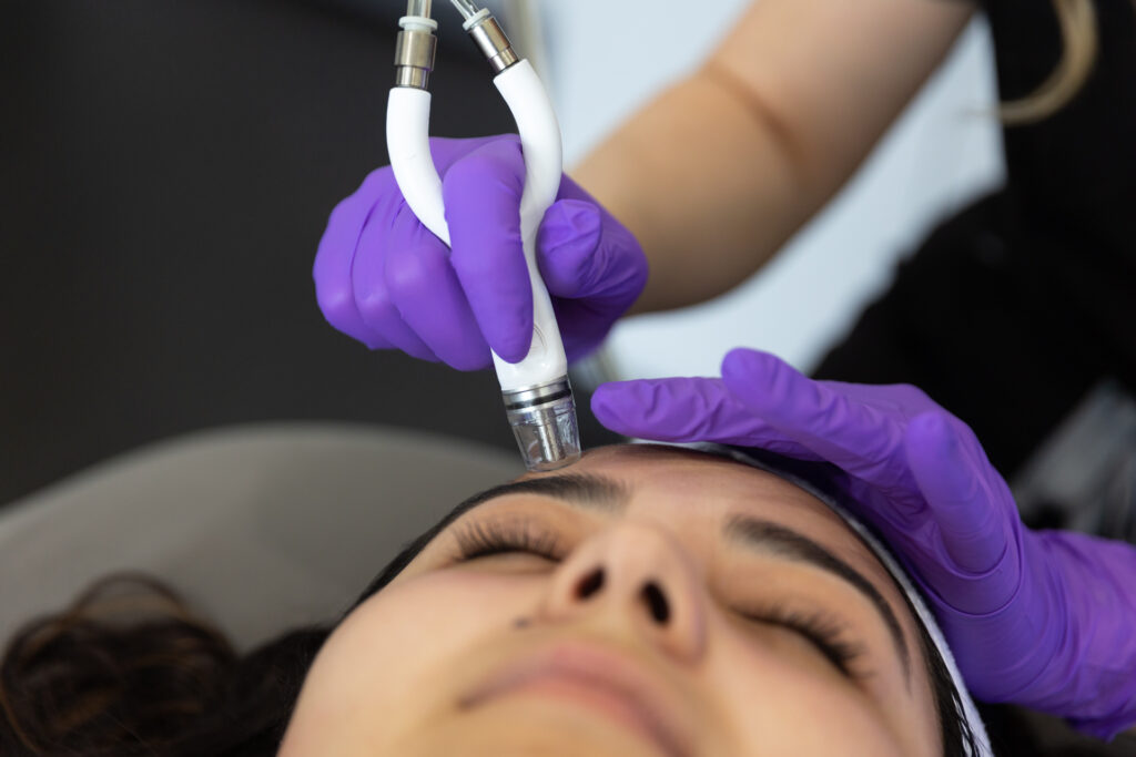 Medium shot of a young woman with dark hair with an aesthetician in purple gloves delviering a DiamondGlow Facial in North Port, FL