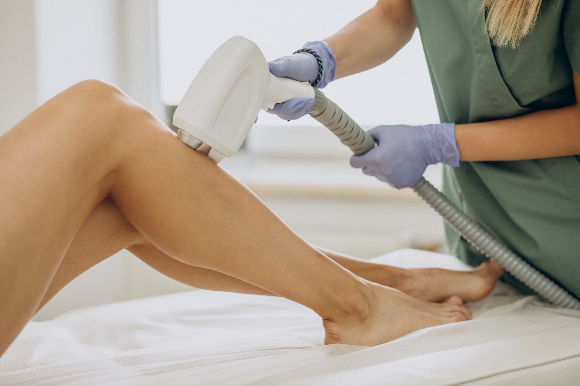 Provider in green scrubs executing the procedure on patient's leg using a larger hand-held device for Laser Hair Removal in North Port