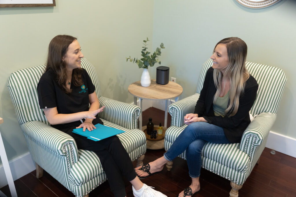A Florida Lakes Spa provider sits down in striped chairs with a patient to discuss her goals and expectations with Emsculpt NEO near Longboat Key.